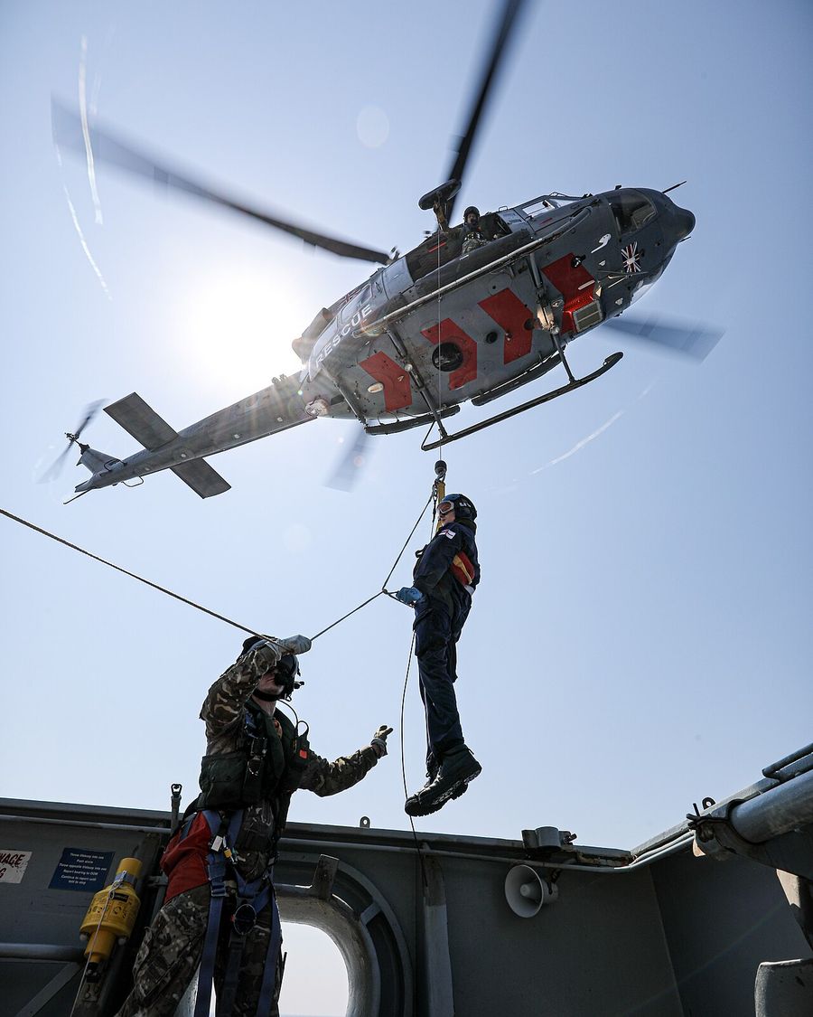 An RAF 84 Squadron helicopter winches a casualty from the deck of HMS Enterprise
